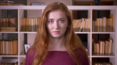 Üniversite kütüphanesinde kameraya bakan genç kızıl saçlı çekici beyaz kız öğrencinin yakın çekim portresi
