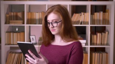 Üniversite kütüphanesinde tablet kullanarak gözlük genç kızıl çekici beyaz kız öğrencicloseup portre