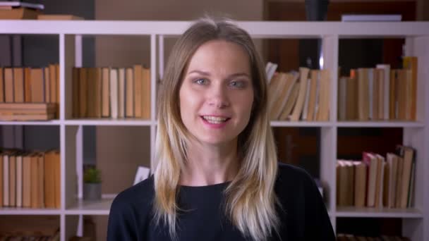 Nahaufnahme einer jungen attraktiven Studentin, die glücklich in die Kamera in der Universitätsbibliothek lächelt — Stockvideo
