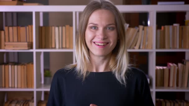 Nahaufnahme einer jungen attraktiven Studentin, die überrascht und aufgeregt in die Kamera in der Universitätsbibliothek blickt — Stockvideo