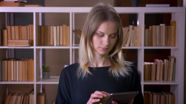 Gros plan de jeune étudiante attrayante utilisant la tablette et montrant l'écran vert à la caméra à l'intérieur dans la bibliothèque de l'université — Video