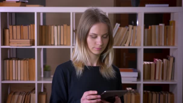Sesión de primer plano de la joven estudiante atractiva usando la tableta y mostrando la pantalla de croma verde a la cámara en el interior de la biblioteca de la universidad — Vídeo de stock