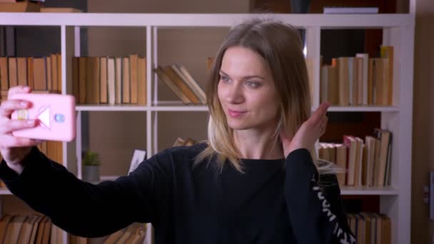 Närbild shoot av unga attraktiva kvinnlig student tar selfies på telefonen inomhus i Universitetsbiblioteket — Stockvideo