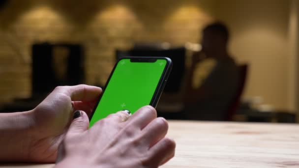 Closeup pohled na ruku ženského pohlaví přidržený telefon se zelenou chromatovou obrazovkou v kanceláři v interiérech — Stock video