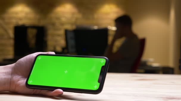 Крупним планом задній перегляд зйомки жіночої руки, що грає відео на телефоні з зеленим хромовим екраном в офісі в приміщенні — стокове відео