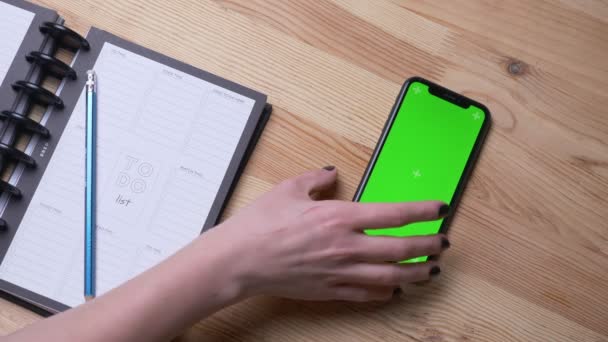 Close-up top shoot van vrouwelijke hand het nemen van een telefoon met groen scherm leggen op het Bureau naast het dagboek binnenshuis in het kantoor — Stockvideo