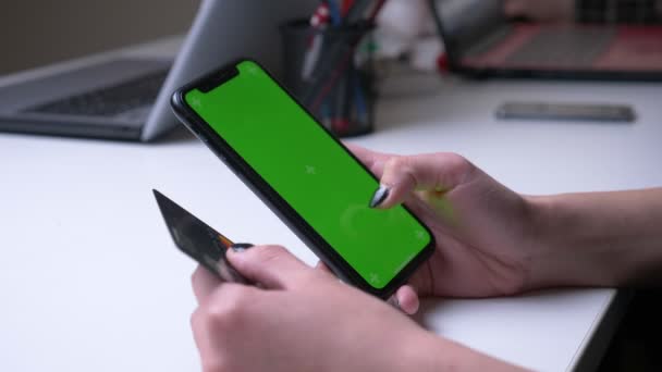 Κοντινό πλάνο της γυναικείας αγοράς χεριών σε απευθείας σύνδεση στο τηλέφωνο με πράσινη οθόνη αποχρώσεων κρατώντας μια πιστωτική κάρτα στο γραφείο σε εσωτερικούς χώρους — Αρχείο Βίντεο