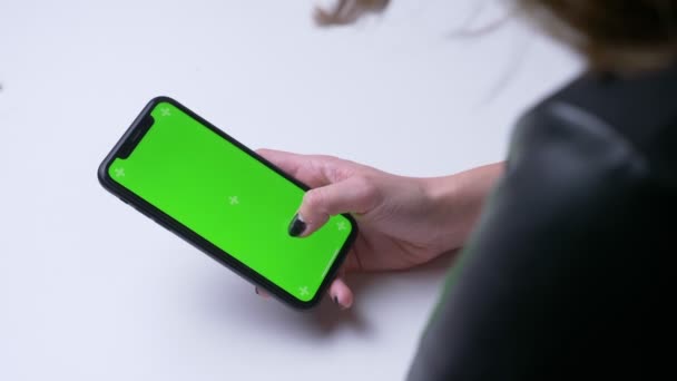 オフィス内のオフィスの屋内で緑色のクロマスクリーンを持つ携帯電話上の女性の手のテキストメッセージのクローズアップバックビュー撮影 — ストック動画