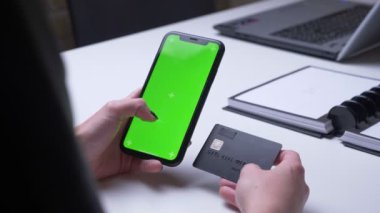Beyaz masada ofiste bir kredi kartı tutan yeşil renk ekran ile telefonda kadın el alışveriş online Closeup geri görünümü ateş