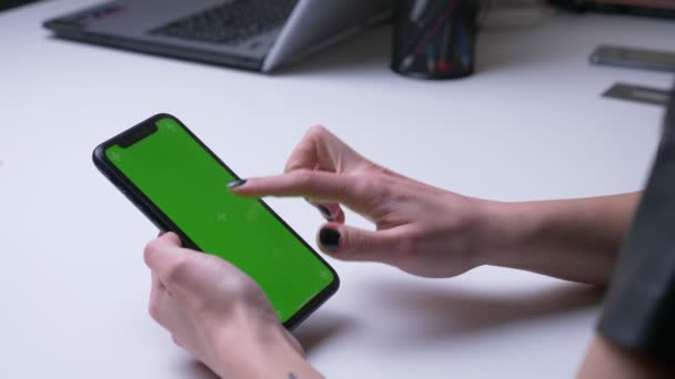 Съемка женской руки с крупным планом на заднем плане, воспроизведение видео приложения по телефону с зеленым хроматическим экраном в офисе в помещении на белом столе — стоковое видео