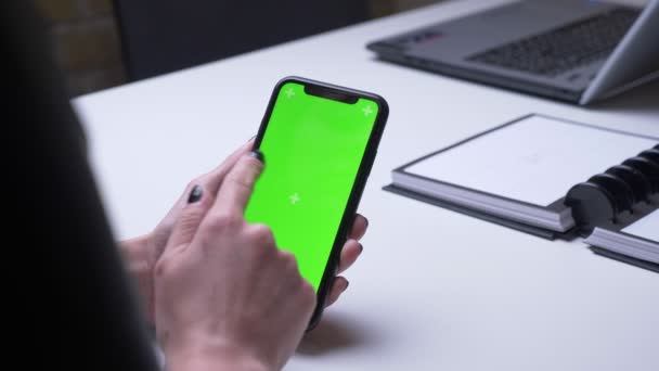 Primer plano de la imagen trasera de la mano femenina jugando una aplicación de vídeo en el teléfono con pantalla de croma verde en la oficina en el interior en el escritorio blanco — Vídeo de stock