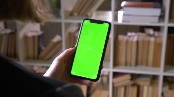 Primo piano vista posteriore ripresa di studenti di sesso femminile mano riproducendo un'applicazione video al telefono con schermo cromatico verde in biblioteca all'interno — Video Stock