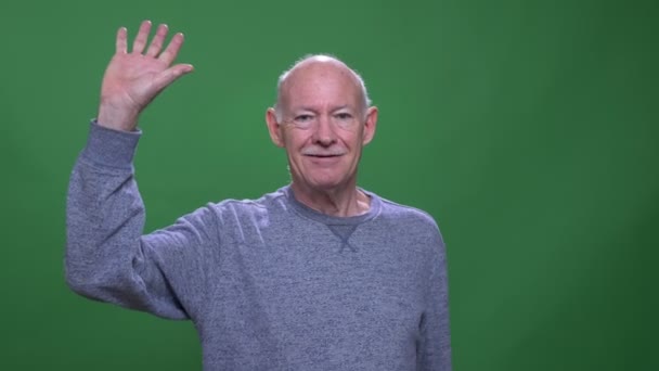 Κοντινό γύρισμα του παλιού καυκάσιο άντρα που χαιρετάει την κάμερα με φόντο απομονωμένο στο πράσινο — Αρχείο Βίντεο