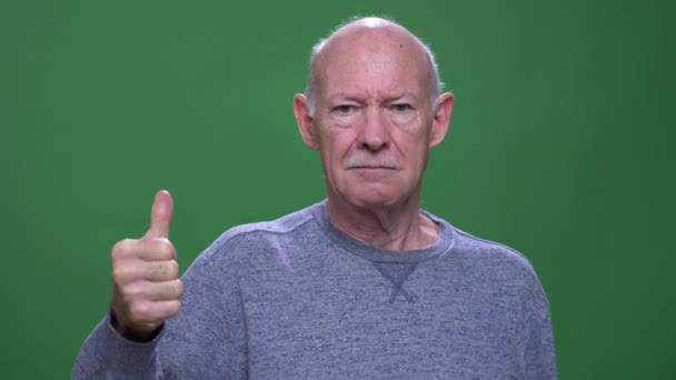 Close-up tiro de idade homem caucasiano sênior mostrando polegar para cima olhando para a câmera com fundo isolado no verde — Vídeo de Stock