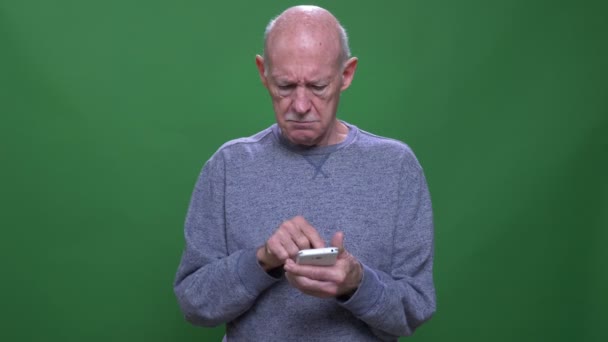 Closeup lő régi magas rangú kaukázusi ember használja a telefont nézi kamera háttérrel izolált zöld — Stock videók