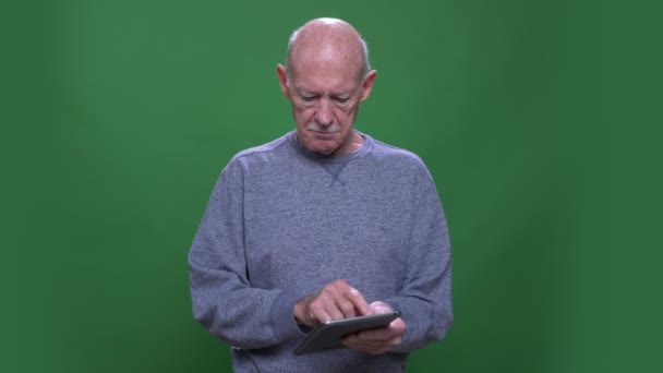 Close-up shoot van oude oudere blanke man met behulp van de Tablet kijken naar camera met achtergrond geïsoleerd op groen — Stockvideo