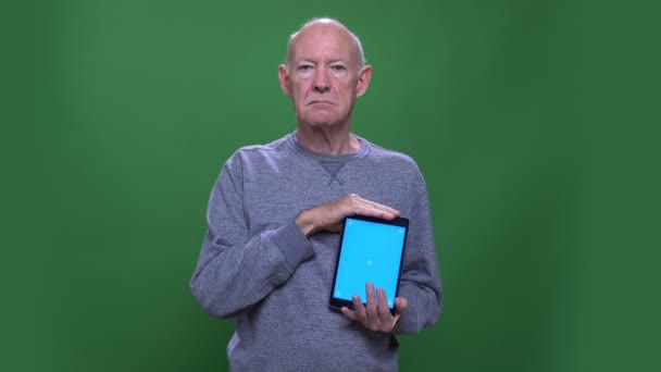 Primo piano di ripresa del vecchio uomo caucasico anziano utilizzando il tablet e mostrando schermo blu guardando la fotocamera con sfondo isolato su verde — Video Stock