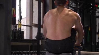 Spor salonunda kapalı tren kürek makinesi kullanarak yetişkin kas atletik gömleksiz adam Closeup geri görünümü ateş