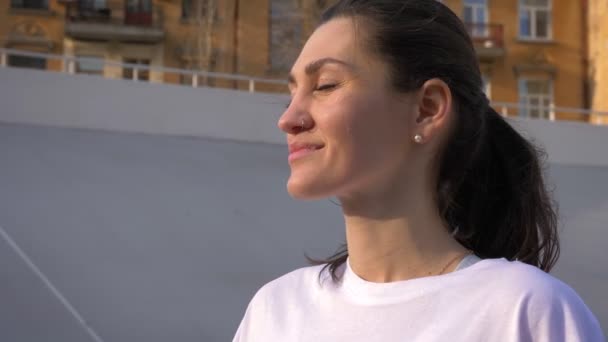 Gros portrait de jeune femme caucasienne en forme de rêve avec queue de cheval souriant et regardant vers l'extérieur sur le stade dans la ville urbaine — Video