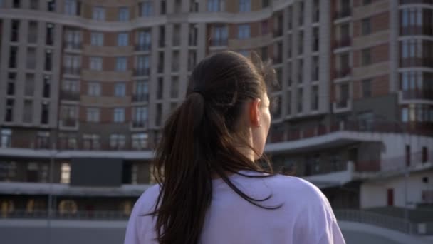 Портрет крупным планом с камерой, движущийся вокруг молодой белой женщины с хвостом, улыбающейся и смотрящей вперед на стадион в городе — стоковое видео