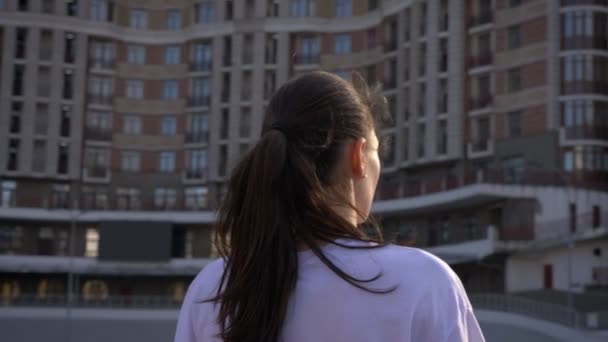 Primo piano ritratto da fotocamera che si muove intorno giovane donna caucasica vestibilità sognante con coda di cavallo sorridente e guardando avanti all'aperto sullo stadio nella città urbana — Video Stock