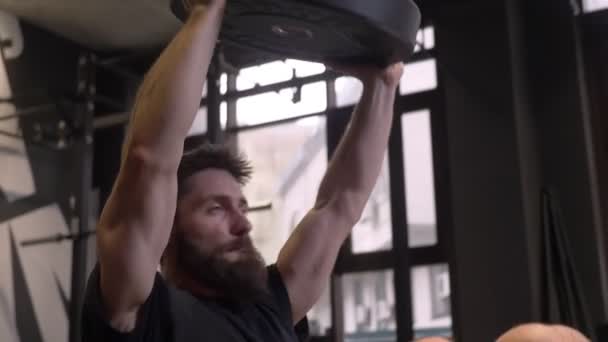 Närbild shoot of Adult muskulös atletisk bodybuilder swingning press och lyft vikter svettas inomhus i gymmet — Stockvideo