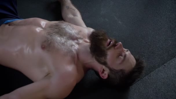 年轻的肌肉无衬衫胡子男子躺在地板上锻炼后，在室内健身房出汗的特写镜头 — 图库视频影像