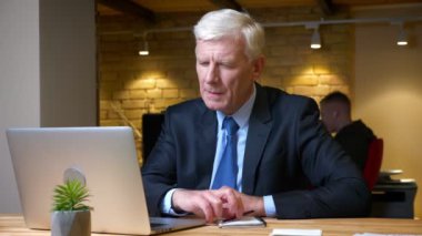 Eski kafkas işadamının dizüstü bilgisayarı kullanarak ve işyerinde ofiste kapalı notlar alarak yakın çekim