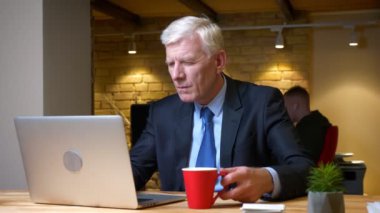 Eski kafkas işadamının dizüstü bilgisayar kullanarak ve kahve içerken meşgul ve işyerinde ofiste kapalı odaklı yakın çekim