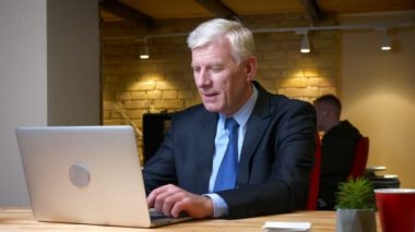 Eski kafkas işadamının dizüstü bilgisayarı kullanarak ve işyerinde ki ofiste ki kapalı mekanlarda memnuniyetle gülümseyerek çekim yaptığı