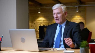 Dizüstü bilgisayarı kullanan ve işyerinde ofiste mutlu olan eski beyaz işadamının yakın çekim çekimi