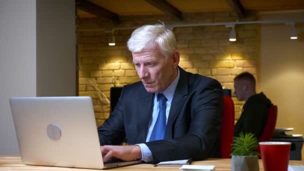 Tiro de close-up do velho homem de negócios caucasiano usando o laptop com dificuldades e frustração dentro de casa no escritório no local de trabalho — Vídeo de Stock