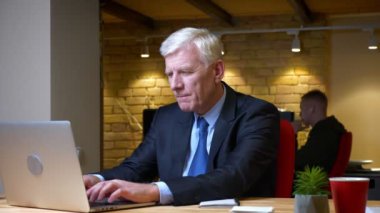 Eski kafkas işadamının kameraya bakmakta güçlük çeken dizüstü bilgisayarı kullanarak ve işyerinde ki ofiste öfkeyle kalem atmanın yakın çekim çekimi