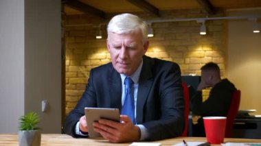 Eski kafkas işadamının tablet arazide gezinirken işyerinin içinde kameranın kapalı mekanlarına baktığı yakın çekim