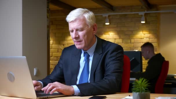 Closeup shoot of old caucasian businessman using the laptop getting a notification on the phone and being happy indoors in the office on the workplace — Stock Video