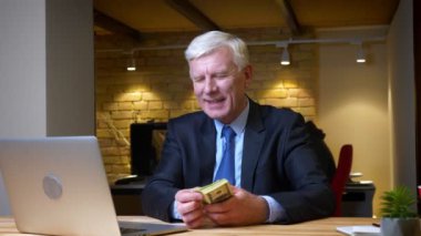 Para sayan eski beyaz işadamının işyerindeki ofiste ki dizüstü bilgisayarın önünde mutlu bir şekilde oturması