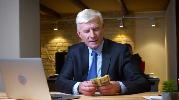 Closeup shoot of old caucasian businessman counting salary sitting in front of the laptop indoors in the office on the workplace — Stock Video