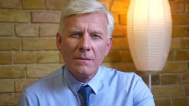 Eski beyaz işadamının kameraya bakıp rahat bir dairede işten sonra evde mutlu bir şekilde gülümsediği yakın çekim portresi