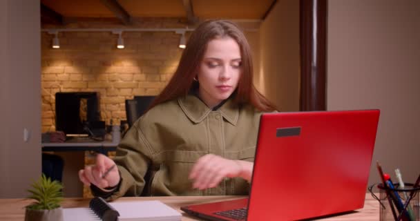 Retrato de la joven adolescente mira en el ordenador portátil con atención haciendo notas en la oficina . — Vídeos de Stock