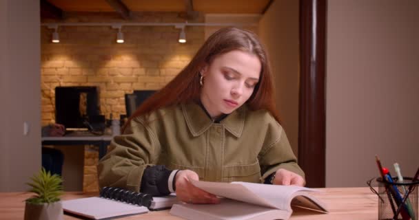 Portrait of young teenage girl reading book attentively writing homework into copybook in office. — Stock Video