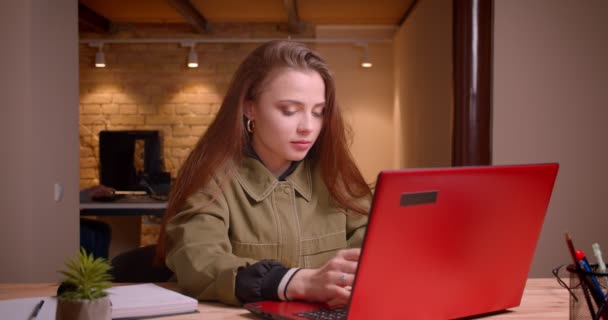 Ritratto di giovane bella ragazza che digita sul computer portatile seduta attentamente in ufficio . — Video Stock