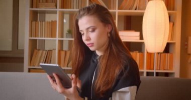 Genç genç kız portre evde kitapraflar arka plan üzerinde kanepede oturan tablet içine saatler.