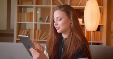 Tablette kitaplıklarda kanepede oturan genç genç kızın portresi arka plan saatler evde kameraya.