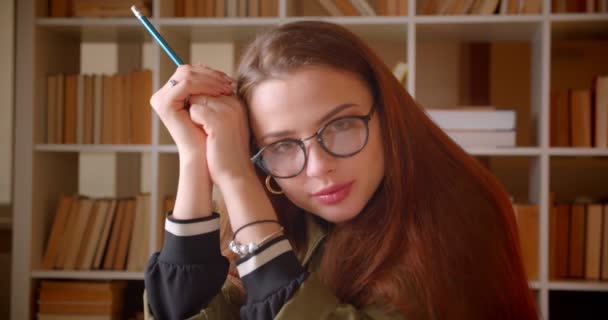 Ritratto ravvicinato di giovane studentessa guarda attentamente nella fotocamera in biblioteca . — Video Stock