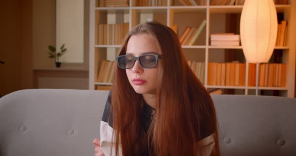 Junges Teenager-Mädchen in 3D-Brille sieht Film im Fernsehen sitzt auf Sofa auf Bücherregalen Hintergrund zu Hause. — Stockvideo
