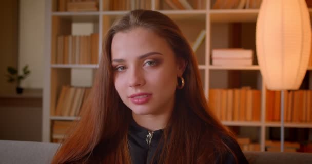 Close-up portret van jonge vrouwelijke student glimlacht in de camera wordt verlegen op bookplanken achtergrond. — Stockvideo