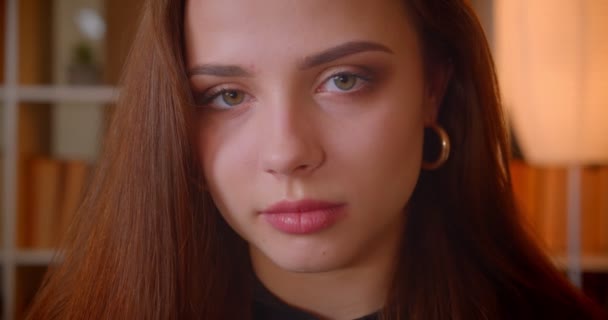 Close-up portrait of young female student smiles into camera being modest and shy on bookshelves background. — Stock Video