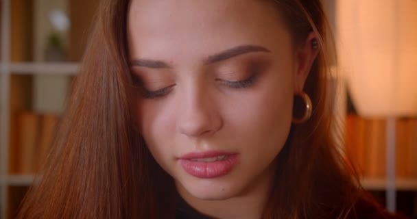 Close-up portrait of young female student watching leftwards smiles into camera being shy and pretty at library. — Stock Video