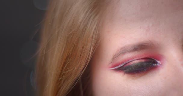 Jedno oko z očí světlého modelu s jasným make-up bliká do kamery, která se upřeně dívá na pozadí bokeh. — Stock video