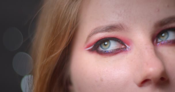 Un brote de ojo de modelo rubia con maquillaje brillante mirando hacia abajo sobre fondo bokeh . — Vídeo de stock